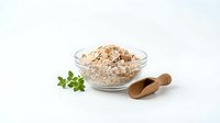 Organic oat flakes in glass bowl with wooden scoop and fresh herbs on white background for healthy breakfast and cooking concepts.