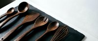 Wooden kitchen utensils set with spoons and whisk arranged on dark slate board for cooking and food preparation.