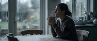 Young woman enjoying hot beverage by window on rainy day, contemplative mood in cozy indoor setting with natural light and peaceful atmosphere.
