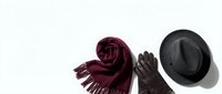 Stylish winter accessories collection featuring burgundy knitted scarf with fringe, brown leather gloves and black felt hat on white background.