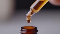 Amber liquid drop falling from glass dropper into bottle, macro photography capturing moment of suspension in alternative medicine and aromatherapy concept.