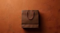 Brown luxury shopping bag with rope handles on textured orange background, suitable for retail, branding, and e-commerce design projects.