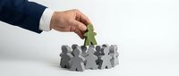 Businessman hand placing green leader figure among gray team members, representing recruitment, promotion, and human resources management strategy.