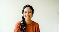 Young woman with long black braided hair and warm smile wearing rust-colored shirt against white background. Suitable for lifestyle, diversity, and portrait projects.