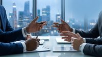 Business professionals exchanging business cards during corporate meeting with city skyline view through office windows at dusk.