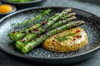 Grilled green asparagus spears with herb butter sauce and pink peppercorns on black ceramic plate. Fresh dill garnish and mustard sauce complement seasonal vegetables.