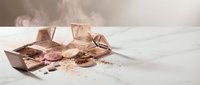 Broken chocolate bar pieces with cocoa powder scattered on white surface creating mess for confectionery and dessert concepts.