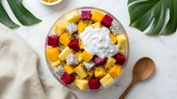Colorful tropical fruit bowl with mango, dragon fruit and berries topped with yogurt cream on white background for healthy breakfast menu design.