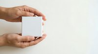 Hands holding blank white box on neutral background for product packaging mockup and branding.