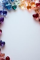Rainbow colored crystal hearts arranged in border frame on white background, creating romantic mood lighting effect with copy space in center.