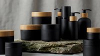 Luxury black cosmetic containers with wooden caps arranged on natural stone surface against neutral background for premium skincare branding.