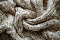 Twisted cream knitted fabric with cable pattern creates soft textural swirls and folds, showcasing intricate wool stitching detail in warm neutral tones.