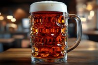 Traditional glass beer mug filled with amber lager showing distinctive dimpled pattern, white foam head on wooden table with blurred pub background.
