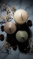 Three scented candles in cream, beige, and sage green arranged on marble with dried flowers and pinecones for home decor and wellness styling.