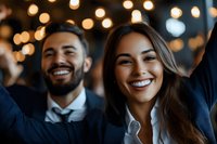 Young diverse business professionals smiling with genuine joy at corporate celebration event. Warm bokeh lights create festive atmosphere in background.