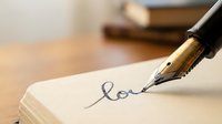 Elegant fountain pen writing love in cursive script on cream paper with warm lighting and blurred books in background creating romantic atmosphere.