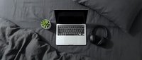 Modern laptop computer with headphones and small plant on dark gray bedding for remote work and digital lifestyle productivity.