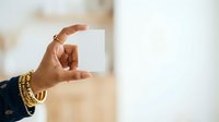 Close-up of hand holding blank white card with gold bracelets, ideal for business cards, invitations, and promotional material presentations.