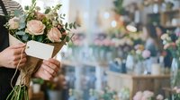 Person holding bouquet of roses and greenery with blank gift tag in flower shop setting.
