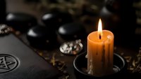 Mystical altar setup with burning orange candle, pentagram book, black stones and ritual elements for spiritual practices and occult ceremonies.