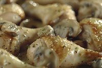 Seasoned chicken wings with herbs and spices in creamy white sauce, close-up macro shot showing texture and glaze. Appetizing party food preparation.