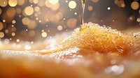 Fresh honey dripping onto golden honeycomb with glowing bokeh lights in background, macro close-up showing detailed texture and natural sweetness in warm amber tones.