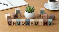 Wooden letter blocks spelling ONBOARDING on office desk with succulent plant, coffee cup, and notebook for business training concepts.