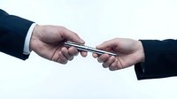 Two businessmen in suits exchanging a silver pen, symbolizing agreement, partnership, and contract signing in a professional setting.