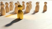 Golden wooden figure standing out from crowd of natural wood pieces on white surface representing leadership, uniqueness and business success concepts.