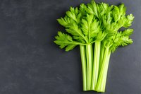 Fresh green celery stalks with leaves arranged on dark background, raw organic vegetable. Clean eating and healthy cooking ingredient for salads and juicing.