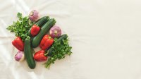 Fresh organic vegetables including red bell peppers, cucumbers, turnips and parsley arranged on neutral background for healthy cooking and nutrition concepts.