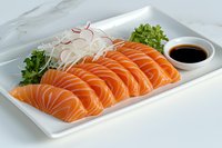 Fresh salmon sashimi slices arranged on white plate with shredded daikon radish, parsley garnish and soy sauce dipping bowl, traditional Japanese cuisine.