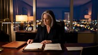 Professional mature Caucasian businesswoman in black suit working late at executive office desk with city lights view through windows at night.