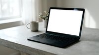 Modern laptop with blank white screen on concrete desk beside coffee cup in bright minimalist workspace for mockup presentations and digital design projects.