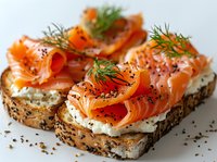 Smoked salmon and cream cheese open sandwiches on seeded bread garnished with fresh dill and black sesame seeds, close up view of gourmet appetizer.