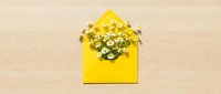 Yellow envelope filled with golden confetti sparkles on wooden background for celebration greeting cards and party invitations.