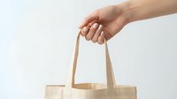 Hand holding eco-friendly beige canvas tote bag on white background. Sustainable shopping concept for zero waste lifestyle and environmental awareness.