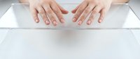 Caucasian female hands touching a transparent glass surface from above, top view, clean minimalist composition on white background.
