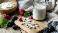 Fresh berries, cashew nuts and glass jar of plant based milk on wooden board with mint leaves, healthy vegan breakfast ingredients.
