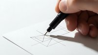 Hand drawing geometric lines on white paper with a black fineliner pen, close-up view of creativity and design process in action.