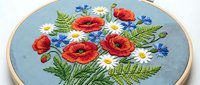 Embroidery hoop with red poppies, white daisies and blue cornflowers on light blue fabric. Handmade needlework craft project for home decor and textile art.