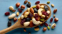 Mixed nuts and dried fruits in wooden spoon on blue background. Healthy snacking, trail mix ingredients including almonds, cashews, cranberries for cooking.