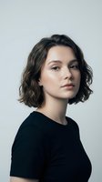 Young Caucasian woman with short wavy brown hair wearing black top against gray background, confident expression for professional headshot photography.