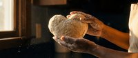 Baker hands holding freshly baked artisan bread loaf in warm kitchen lighting. Traditional bakery craftsmanship and homemade baking concept.