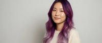 Young Asian woman with purple ombre hair smiling warmly at camera wearing casual white top against neutral background for lifestyle content.