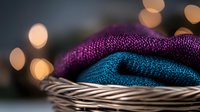 Folded knit sweaters in purple and turquoise stacked in woven basket with warm bokeh lights, perfect for fashion, textile, and lifestyle design projects.