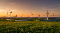 Wind turbines and solar panels in green field at sunset generating renewable energy for sustainable power production.