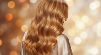 Luxurious golden blonde wavy hair cascading down woman's back with warm bokeh lights creating glamorous salon atmosphere for beauty and haircare concepts.