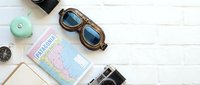 Vintage travel accessories flat lay with retro aviator goggles, camera, compass and map on white wooden background for adventure planning and wanderlust concepts.