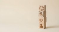 Wooden blocks with business icons including smiley face, recycling symbol, handshake and person stacked vertically on neutral background for corporate concepts.